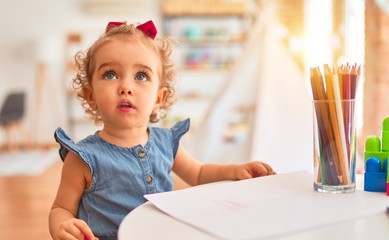 Beautiful caucasian infant playing with toys at colorful playroom. Happy and playful drawing with color pencils at kindergarten.