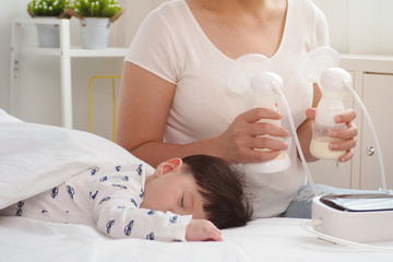 Asian mother holding twin breast pump after feeding her baby in the bedroom at home