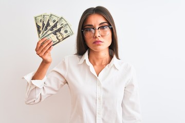 Beautiful businesswoman wearing glasses holding dollars over isolated white background with a confident expression on smart face thinking serious