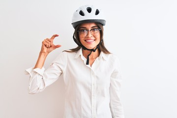 Beautiful businesswoman wearing glasses and bike helmet over isolated white background smiling and confident gesturing with hand doing small size sign with fingers looking and the camera