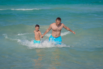 European man and his son are swimming in the ocean together during their vacations. Healthy lifestyle.