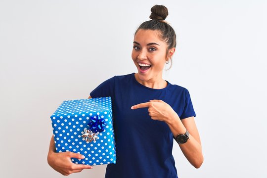 Young beautiful woman holding birthday gift standing over isolated white background very happy pointing with hand and finger
