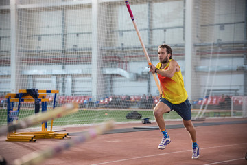 Pole vaulting indoors - a athletic man in yellow shirt running on the track with a pole in the...