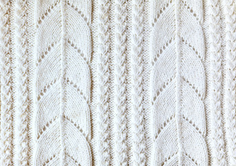Needlework, knit and craft. Texture of hand-knitted pullover of light milk color from natural merino wool. Volumetric background ornament, resembling leaves and stripes. Top view, close up, flat lay