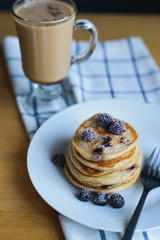 small circular fritter or pancakes with blackberry, frozen berries, fork on plate and coffee on checkered napkin, russian breakfast, closeup view from above of vertical life style stock photo image