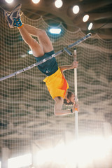 Pole vaulting training in the sports stadium - an athletic man jumping over the bar
