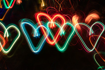 Row of multicolored neon glowing hearts on black background.