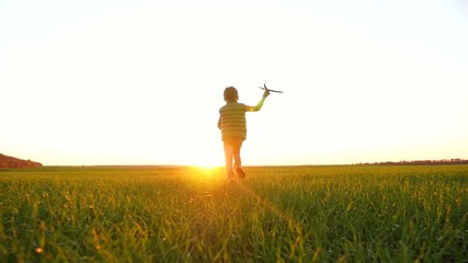 A happy little boy runs across a green meadow playing with a toy airplane, imagining flying. - Powered by Adobe