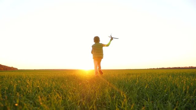 A happy little boy runs across a green meadow playing with a toy airplane, imagining flying.