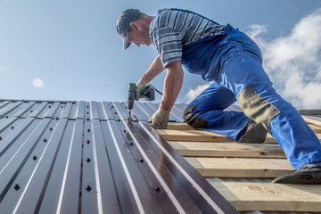 male builder performs work on the roof, fastens corrugated sheets О