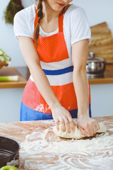 Young brunette woman cooking pizza or handmade pasta in the kitchen. Housewife preparing dough on wooden table. Dieting, food and health concept