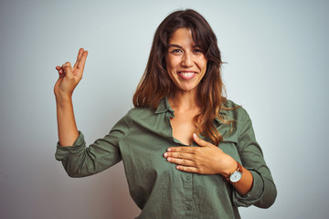 Young beautiful woman wearing green shirt standing over grey isolated background smiling swearing...