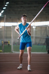 Obraz premium Pole vault training in the sports stadium - young man standing on the track holding a pole and looking up