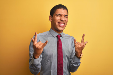 Young handsome arab businessman wearing shirt and tie over isolated yellow background shouting with crazy expression doing rock symbol with hands up. Music star. Heavy concept.