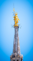 Gold religious statue at the top of the Milan cathedral.