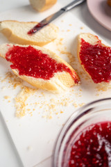 Fresh sliced ​​baguette and sweet raspberry jam for vitamin breakfast on a white table in the kitchen. Close-up. Vertical