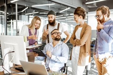 Senior manager having a meeting with office workers standing together near the working place in the modern office. Concept of a small conference and teamwork