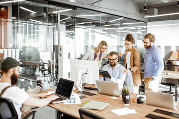 Group of diverse colleagues working on the computers in the modern office or coworking space, bearded hipster as a programmer writing code