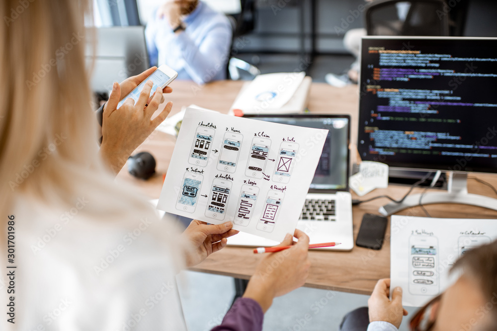 Wall mural developers or web designers developing mobile application in the office, close-up on phone and paper