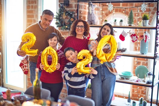 Beautiful family smiling happy and confident. Standing and posing holding 2020 balloons celebrating new year at home