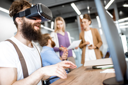 Young people working in the office, creative bearded man trying a new product or playing game with virtual reality goggles