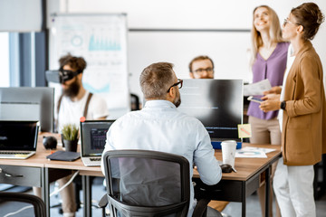 Group of diverse colleagues working with computers in the modern office or coworking space, writing programming code and working with vr goggles