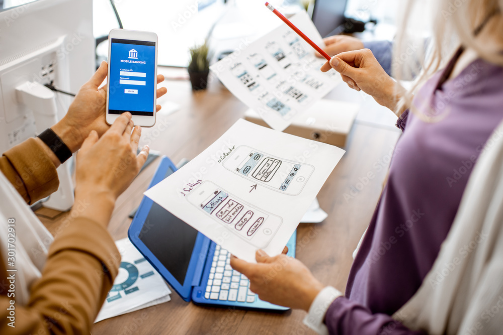 Wall mural developers or web designers developing mobile application for banking in the office, close-up on pho