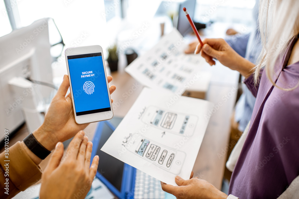 Wall mural developers or web designers developing mobile application for banking in the office, close-up on pho