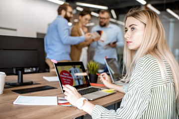Portrait of a young woman as a web designer in the office with coworkers on the background