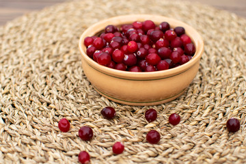 Close up clay bowl full of cranberries with spread of red berries at the table in the morning in countryside during breakfast at wicker napkin