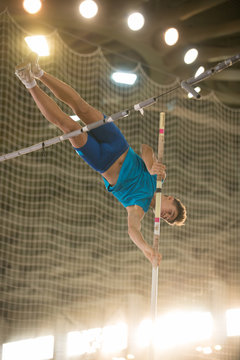 Pole vaulting - guy is jumping over the bar holding on to a pole