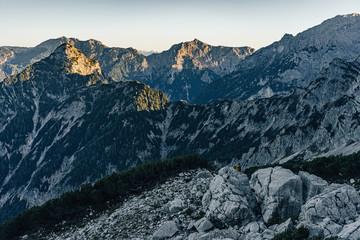 Fototapeta premium Beautiful sunset view of a mountain alpine landscape of Totes Gebirge, Austria. High alpine peaks in yellow and orange evening light. Rocky summit and rock walls of alpine peaks. Blue sky.