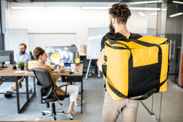Courier delivering products for office workers, carrying yellow thermal bag, view from the back...