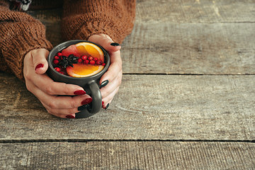 Woman's hands in warm sweater holding a cup of mulled wine