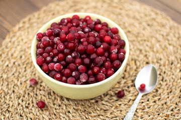Healthy breakfast in big green bowl full of frozen cranberry, metal spoon and spread berries at wooden table covered by wicker napkin in the village