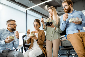 Group of diverse colleagues eating takeaway salad, sitting together and having fun during a...