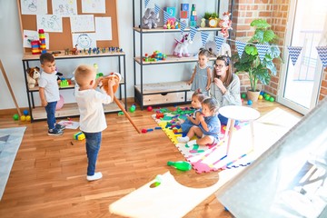 Beautiful teacher and group of toddlers playing around lots of toys at kindergarten