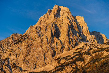 Fantastic view of a alpine mountain landscape of Totes Gebirge and the summit of Spitzmauer. Big rock wall, blue sky and mountains lid with orange sun. Sunrise or sunset mountain landscape, Austria.