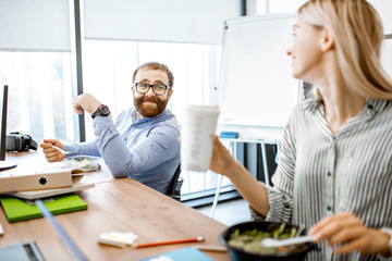 Man and woman eating salad and drinking coffee during a lunch time on the working place without leaving the office