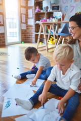 Obraz premium Beautiful teacher and group of toddlers sitting on the floor drawing using paper and pencil around lots of toys at kindergarten