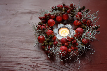 Natural wreath with rose hips and small apples around a burning candle on a red wooden table, seasonal decoration in autumn, Advent and Christmas time - Powered by Adobe