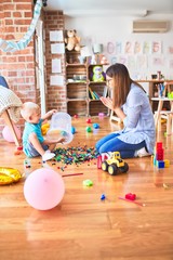 Fototapeta premium Young caucasian child playing at playschool with teacher. Mother and son at playroom bulding a tower with toy blocks