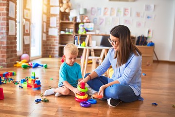 Young caucasian child playing at playschool with teacher. Mother and son at playroom with intelligence toy