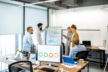 Group of diverse colleagues discussing some working momets with presentation on flipchart during a small conference in the office