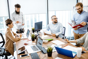 Group of diverse colleagues working in the modern office, having discussion or small conference on a working place with computers