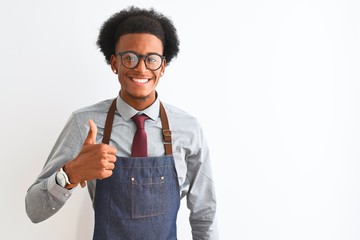 Young african american shopkeeper man wearing apron glasses over isolated white background doing happy thumbs up gesture with hand. Approving expression looking at the camera showing success.