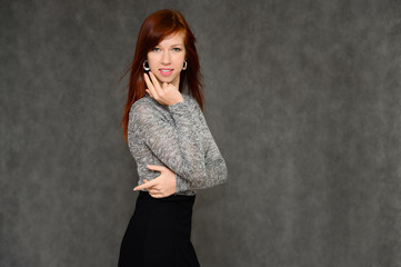 Portrait of a pretty woman, red-haired girl with long smooth hair on a gray background in a gray dress. Talking to the camera, showing joy and surprise, smiling.