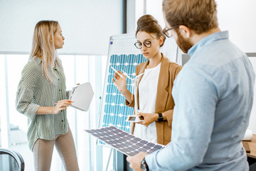 Young group of engineers working on a project of alternative energy in the office, holding model of...
