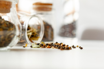 Glass jars with dry tea leaves close up on white table