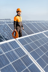 Well-equipped worker in protective orange clothing servicing solar panels on a photovoltaic rooftop plant. Concept of maintenance and installation of solar stations